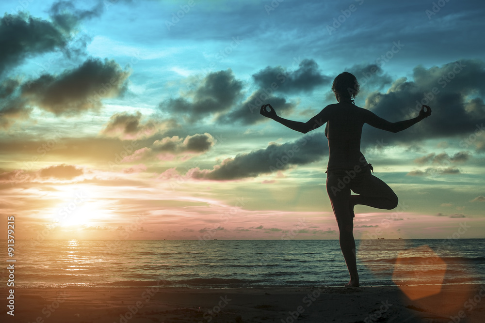 Fototapeta premium Silhouette of young women standing at yoga pose on the beach during an amazing surreal sunset.