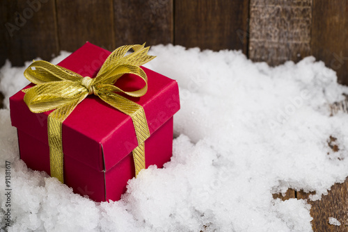 Christmas gift box with a gold ribbon bow on snow