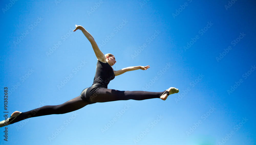 Fototapeta premium Smiling young gymnast is jumping in split and floating above the