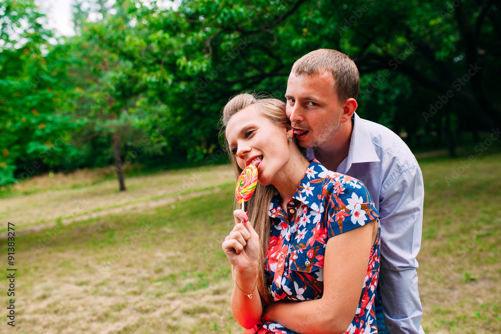 Fototapeta premium Lollipop fun. Young loving couple tasting multi colored lollipop