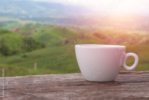 White coffee cup on wooden table with mountains view