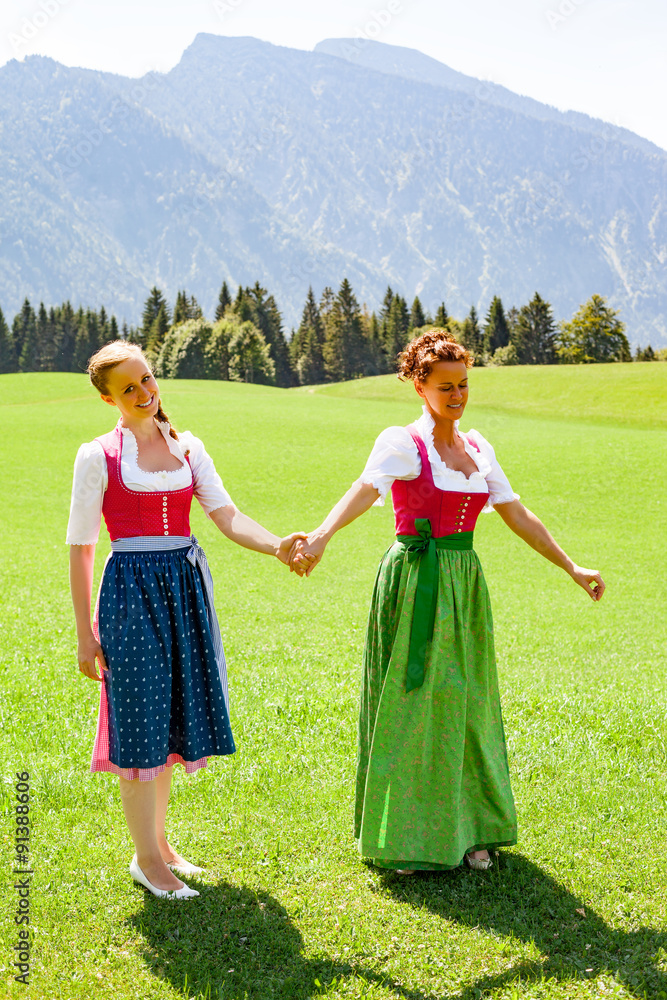 Mutter und Tochter beide im Dirndl gehen Hand in Hand spazieren. Mutter und Tochter beide im Dirndl gehen Hand in Hand spazieren.