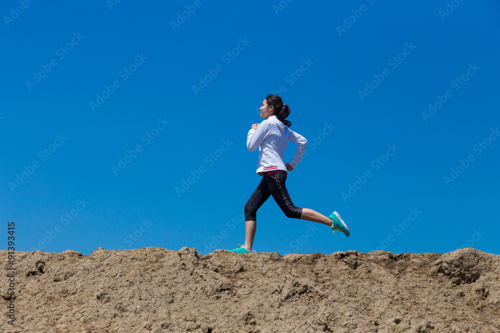 young woman running on mountain trail with blue sky background young woman running on mountain trail with blue sky background