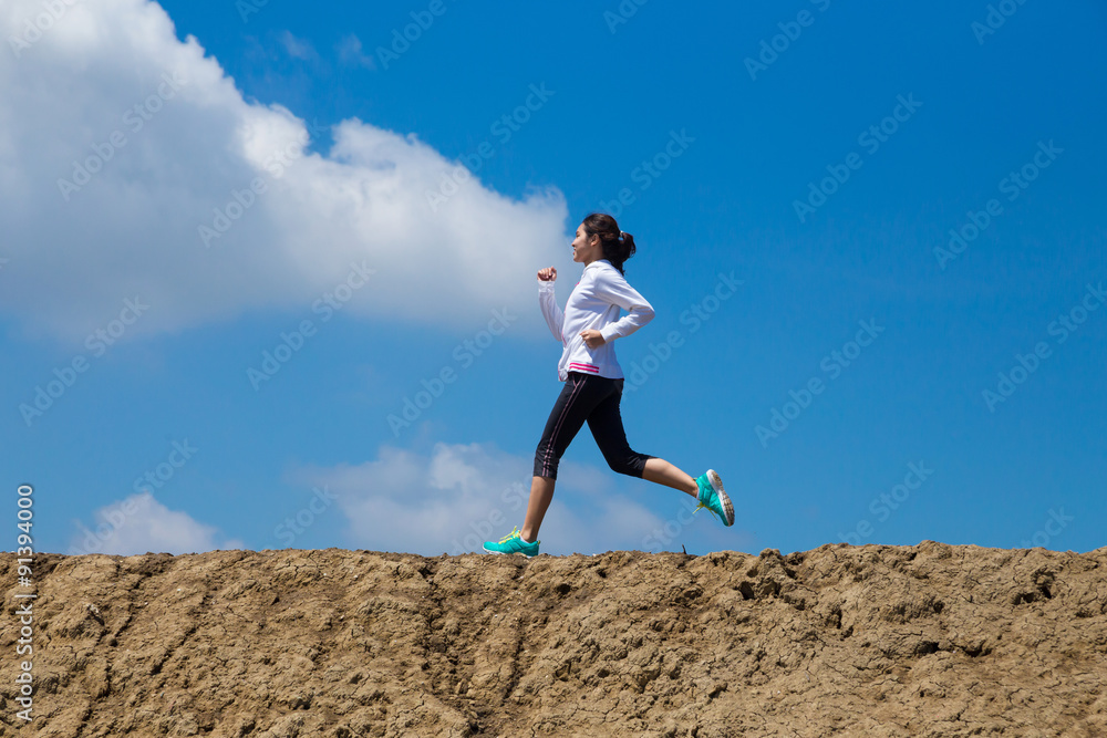 young woman running on mountain trail with blue sky background young woman running on mountain trail with blue sky background