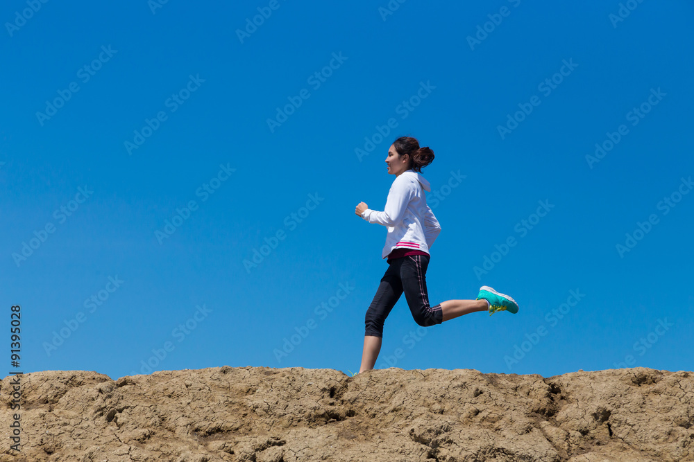young woman running on mountain trail with blue sky background young woman running on mountain trail with blue sky background