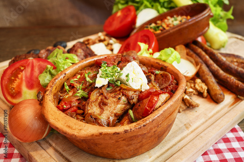 Meat and vegetable in ceramic pot on wooden plank