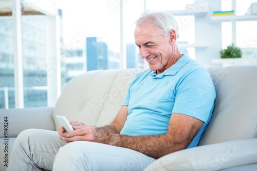 Happy senior man using smartphone while sitting on sofa