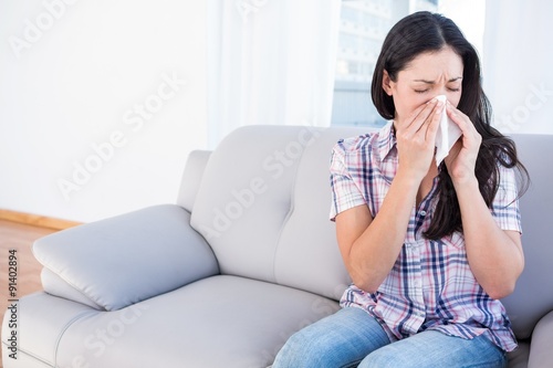 Фотография Pretty brunette sneezing on tissue on couch