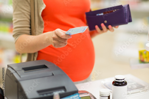 pregnant woman with money at cashbox in drugstore