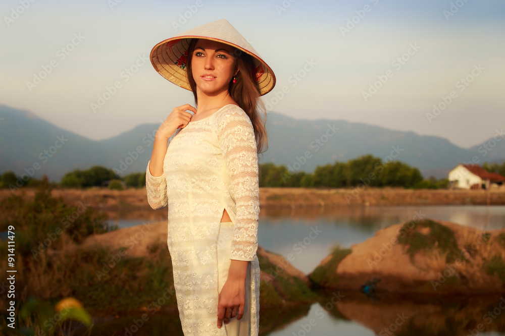 girl in Vietnamese hat against lakes house mountains