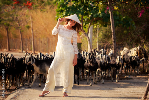 blonde girl in Vietnamese dress touches hat against flock