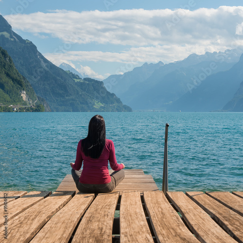 Relaxation. Woman sitting in lotus position and meditating on the lake. 