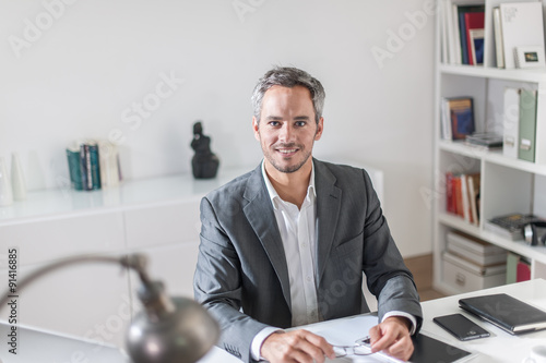 Εκτύπωση καμβά Grey hair businessman with a beard wearing a grey suit. He is si