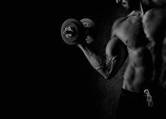 Handsome muscular man working out with dumbbells over black back