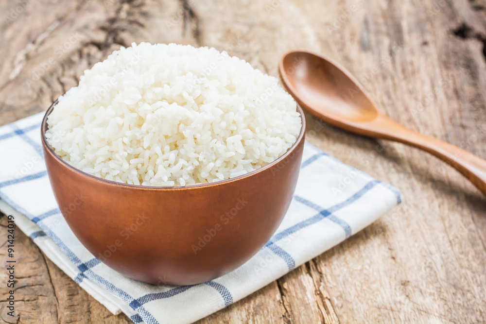 Cooked rice in bowl with spoon and dishcloth on old wooden table Cooked rice in bowl with spoon and dishcloth on old wooden table