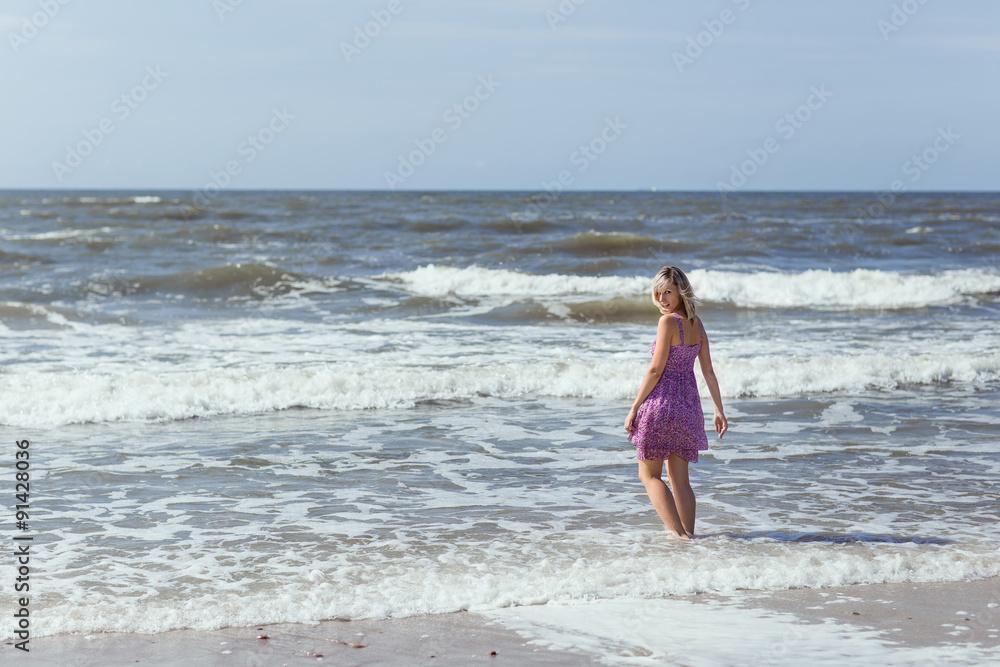 Young beautiful slim girl standing on the beach on a sunny summer day, a strong wind on the sea Young beautiful slim girl standing on the beach on a sunny summer day, a strong wind on the sea