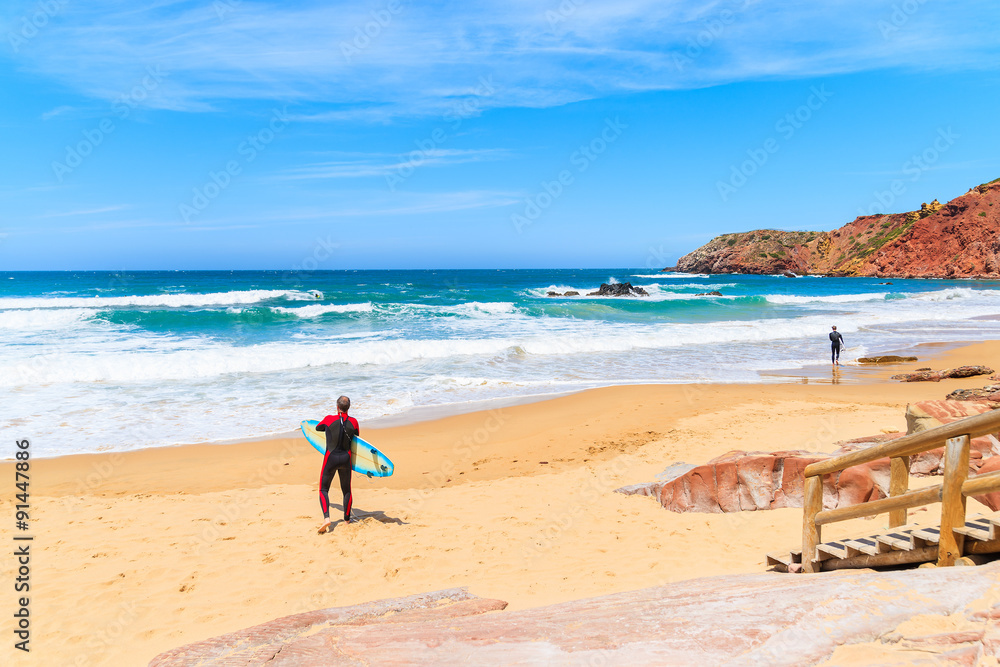 Surfer standing on Praia do Amado beach with ocean waves hitting shore, Algarve region, Portugal Surfer standing on Praia do Amado beach with ocean waves hitting shore, Algarve region, Portugal