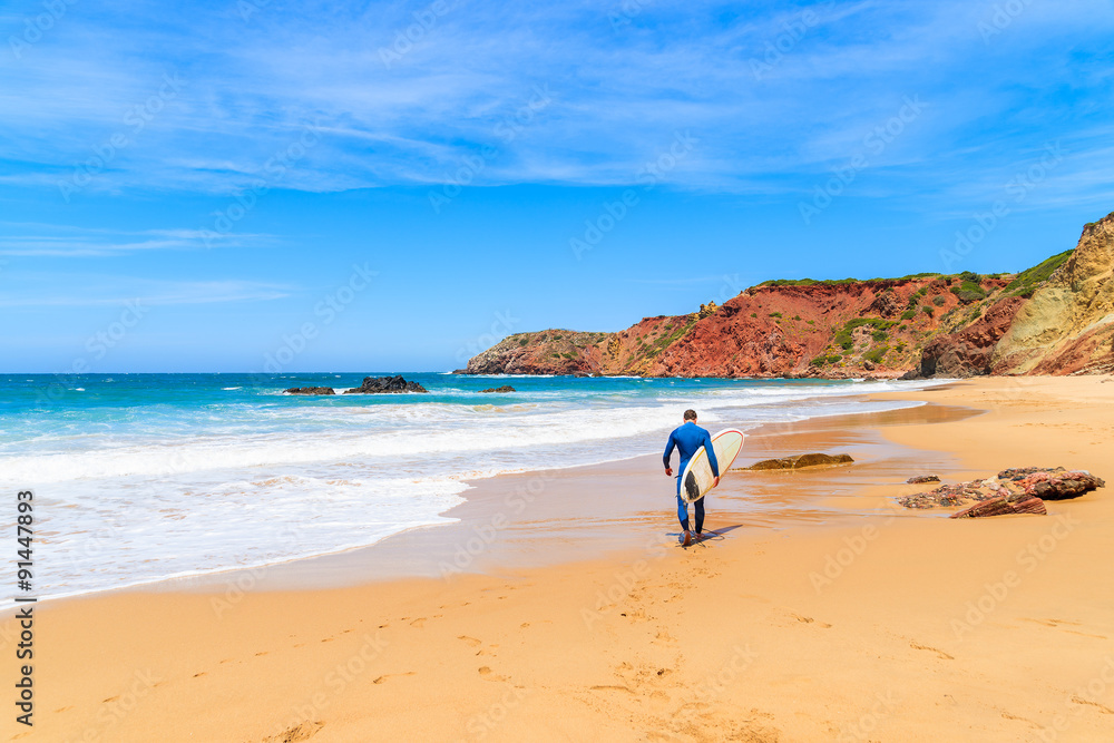 Surfer walking on Praia do Amado beach on sunny summer day, Algarve region, Portugal