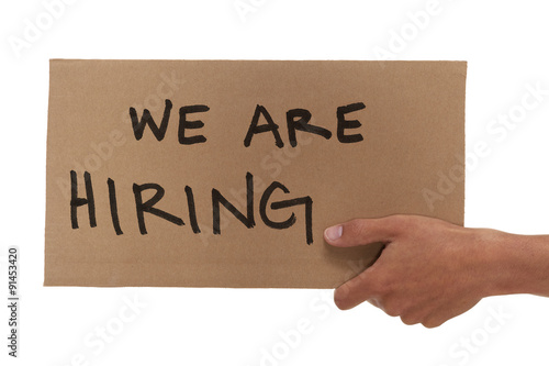 Hand holding up a cardboard we are hiring sign