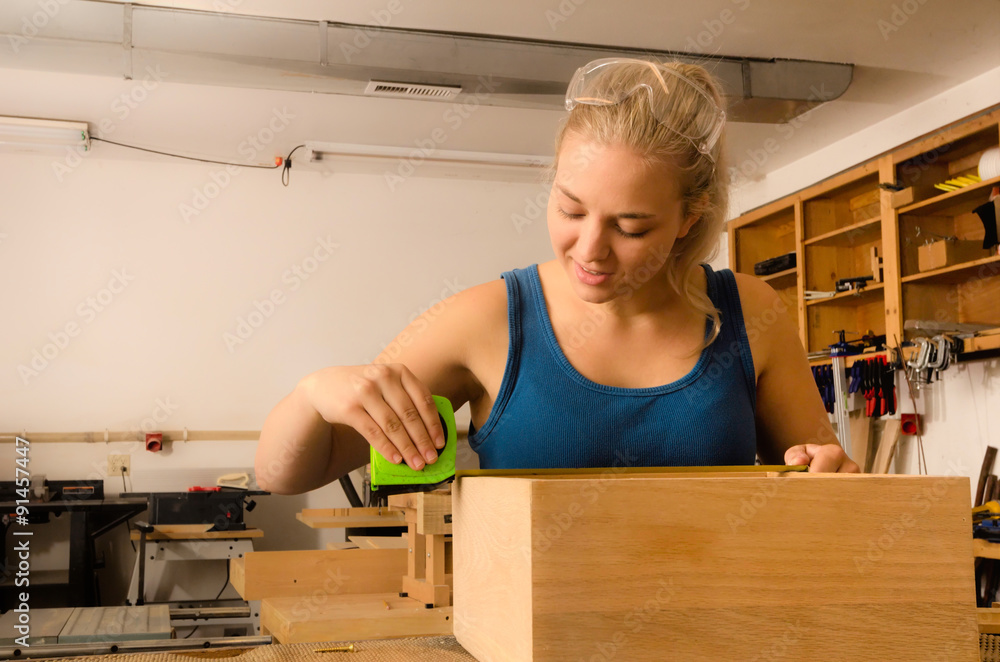 Young adult female woodworker measuring an oak box with a tape measure. Young adult female woodworker measuring an oak box with a tape measure.