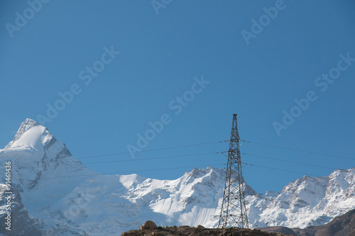 Single electricity pole with snow mountain background and blue sky © beebright