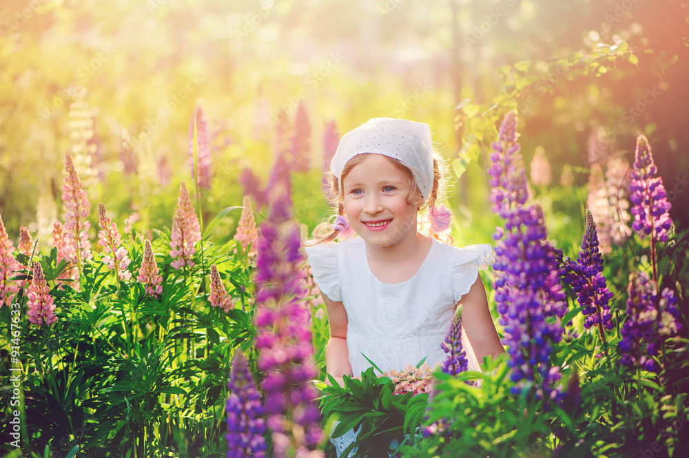 cute happy child girl on the walk on summer lupin flower field