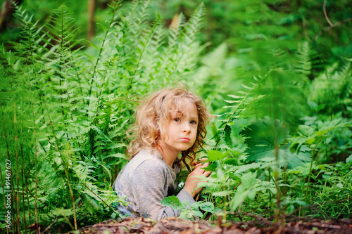 child girl hiding in wild ferns in summer forest