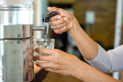 Woman hand pouring water in to clear glass