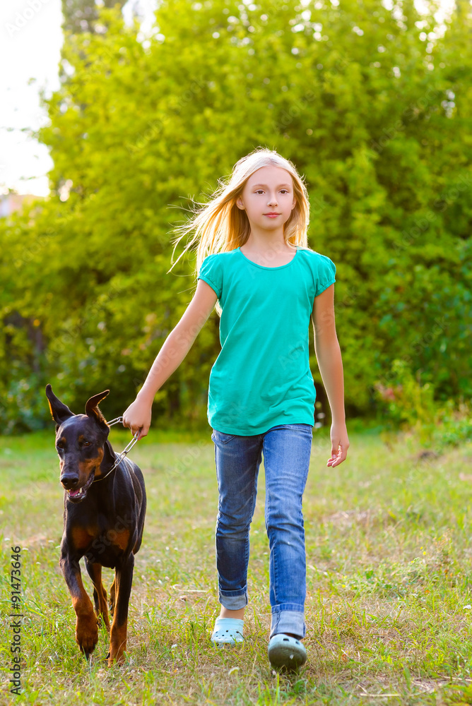 blonde girl walking with the dog or doberman in summer park