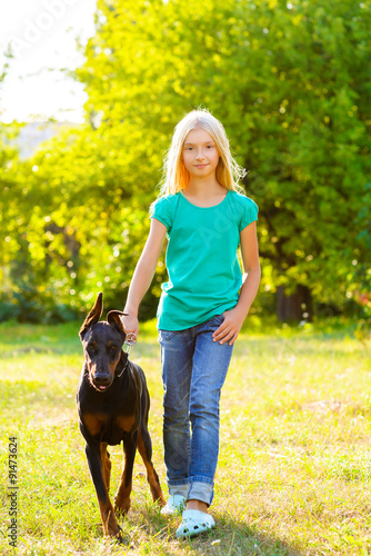 blonde girl walking with the dog or doberman in summer park