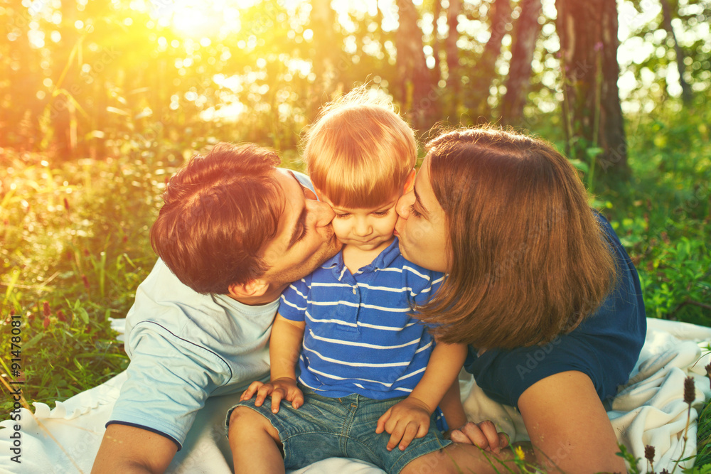 Fototapeta premium Happy parents kissing their child outdoors