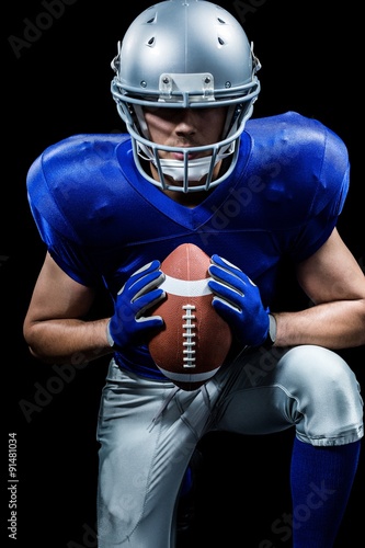 Determined American football player holding ball while kneeling