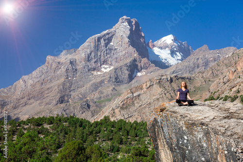 Young woman doing exercise Female Athlete Sitting in Yoga Zen Mediation Pose Mountain Panoramic Landscape Outdoor Orange Rocks Green Forest Clear Blue Sky High Summit Shining Sun
