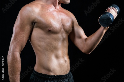 Midsection of shirtless athlete working out with dumbbell