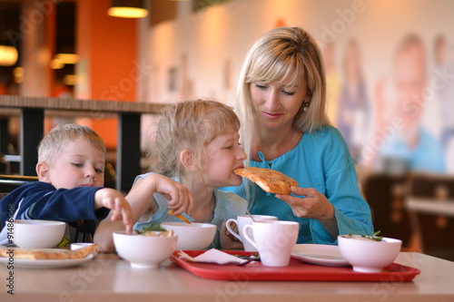 The young woman and two children eat in cafe
