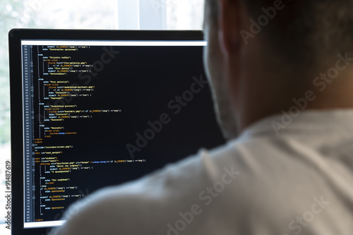 programmer from behind and programming code on computer monitor photo