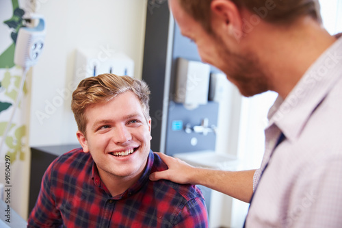 Male Patient Being Reassured By Doctor In Hospital Room