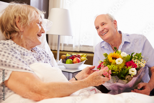 Husband Visiting Senior Wife In Hospital With Flowers © Monkey Business