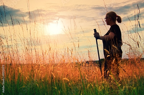 "ong hair girl is walking through meadow at amazing golden sunset background.