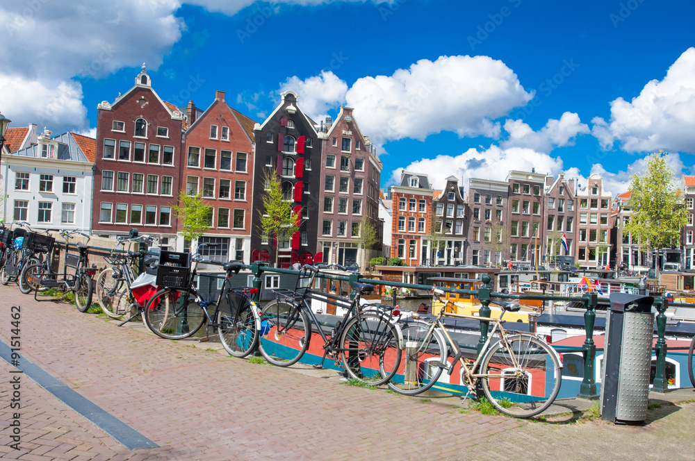 Naklejka premium Amsterdam, the Netherlands-April 27: Amsterdam cityscape with apartment houses and bikes parked on the bridge on April 27,2015. Amsterdam is the most populous city of the Kingdom of the Netherlands.
