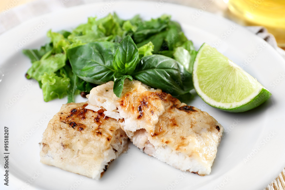 Dish of fish fillet with greens and lime on table close up Dish of fish fillet with greens and lime on table close up