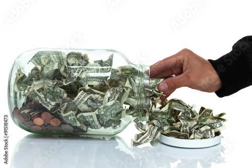 Glass jar full of money tipped over on its side spilling money w