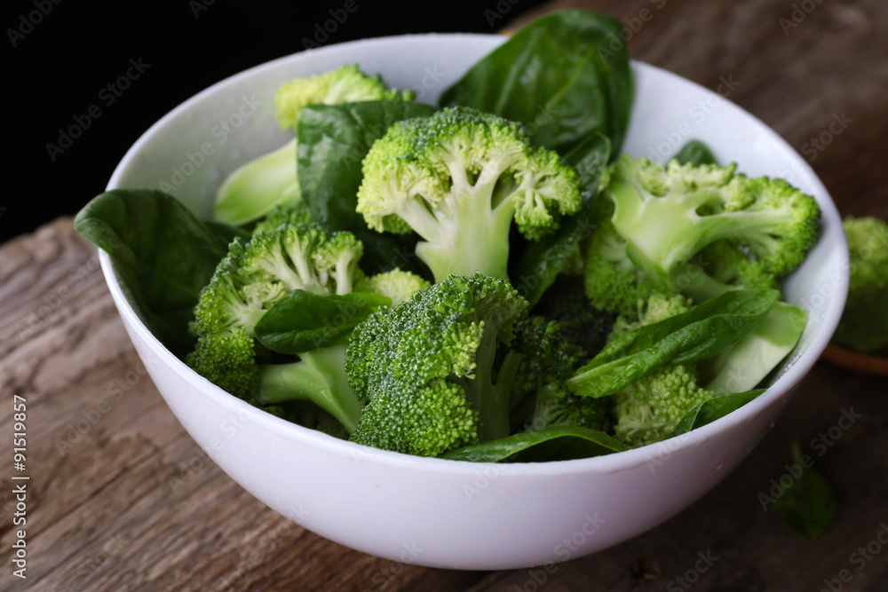 Fresh broccoli with spinach in bowl on wooden table close up Fresh broccoli with spinach in bowl on wooden table close up