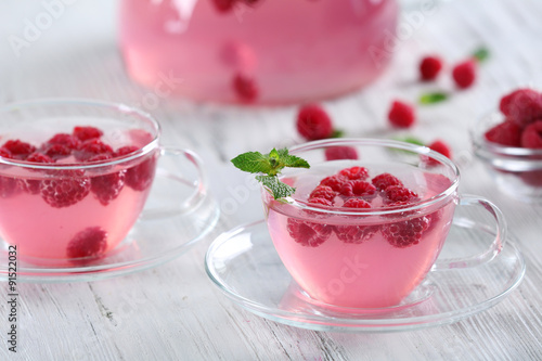 Cups and teapot of raspberry drink with berries on wooden table close up