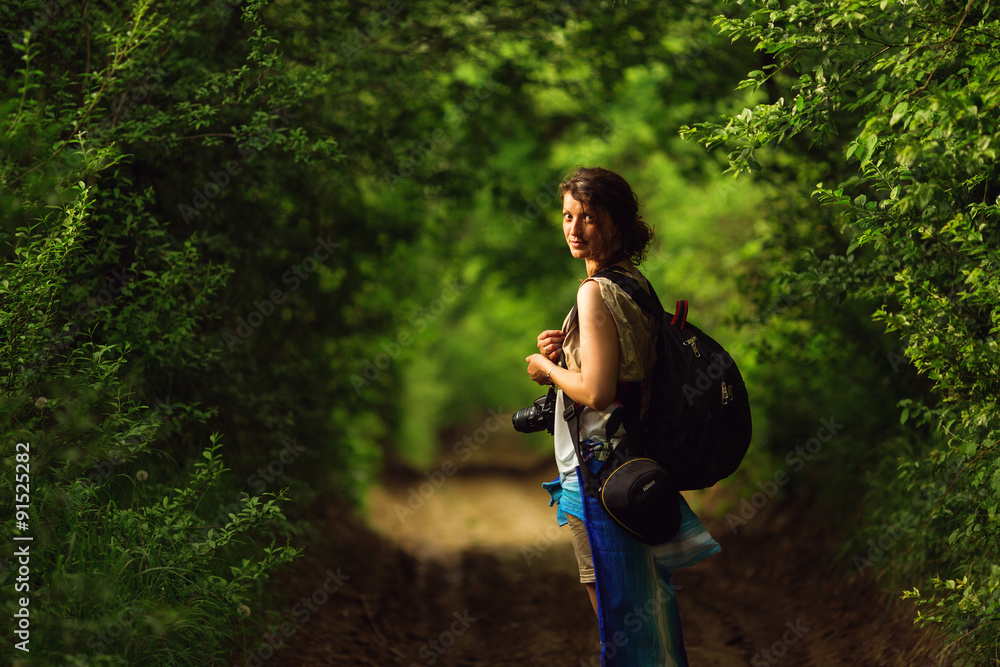 Young female hiker walking in beautiful forest nature landscape in mountains. Woman hiker wearing backpack looking at camera. Young female hiker walking in beautiful forest nature landscape in mountains. Woman hiker wearing backpack looking at camera.