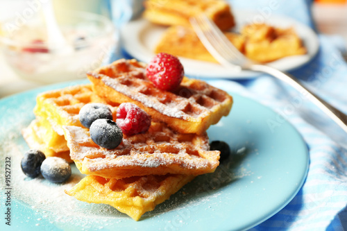 Sweet homemade waffles with forest berries on plate, on light background
