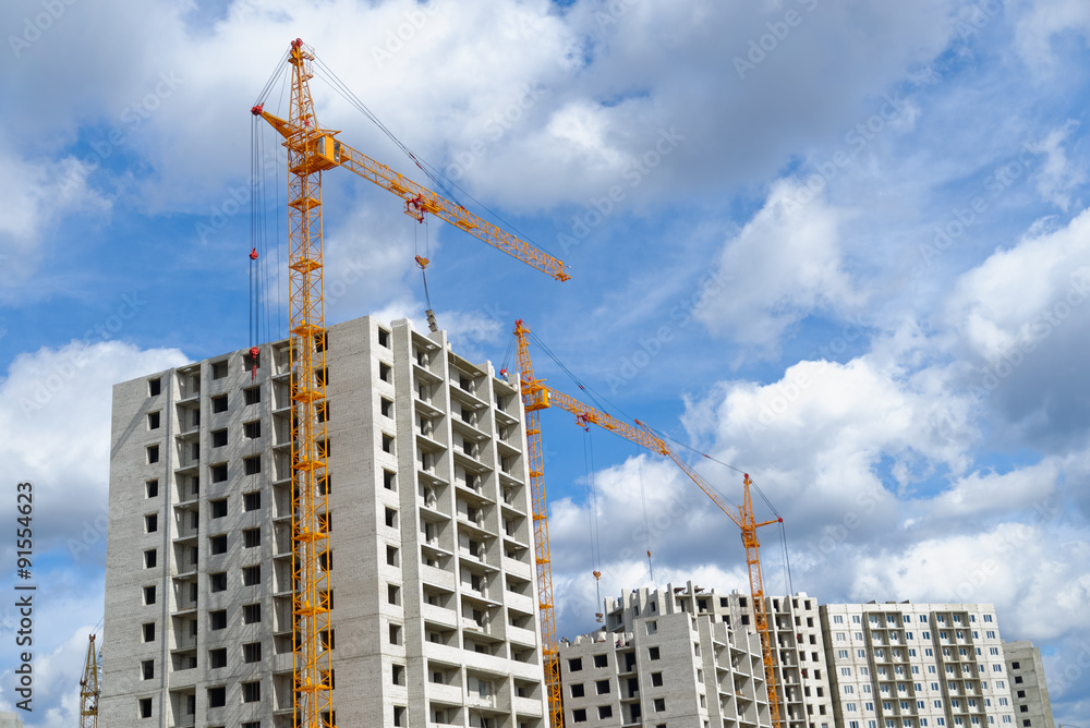 Fototapeta premium Hoisting cranes and multi-storey housing under construction