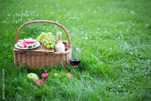 Fototapeta Naklejka Na Ścianę i Meble -  picnic basket with fruits and glass of wine on green grass