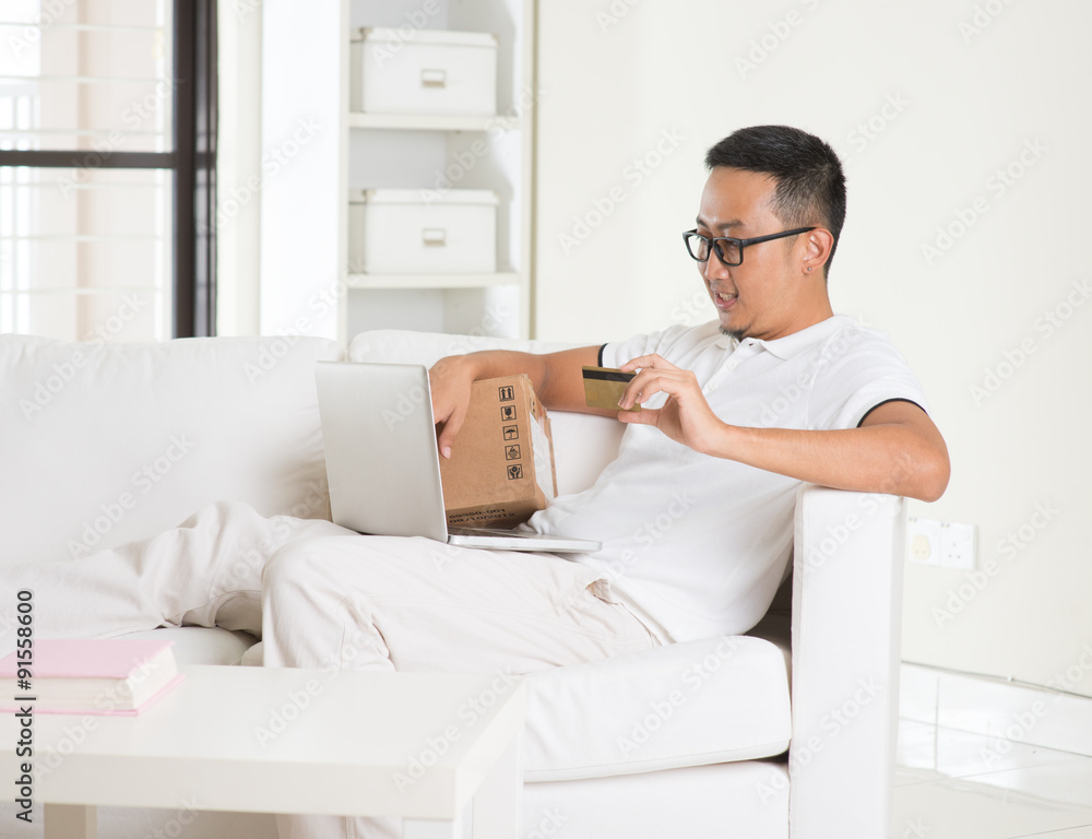 casual asian man online shopping in livingroom