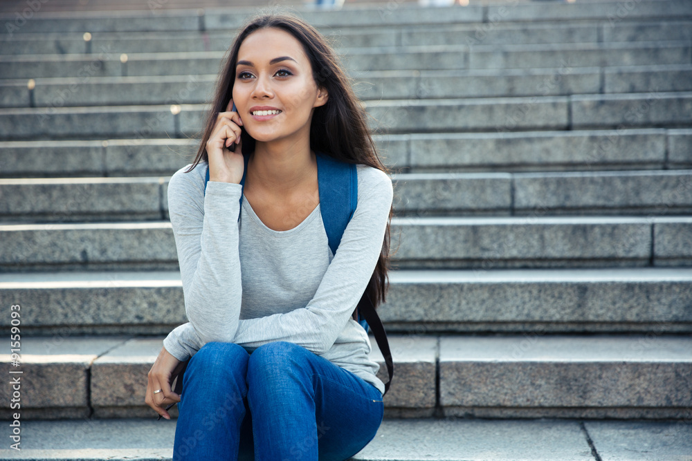 Smiling female student talking on the phone outdoors